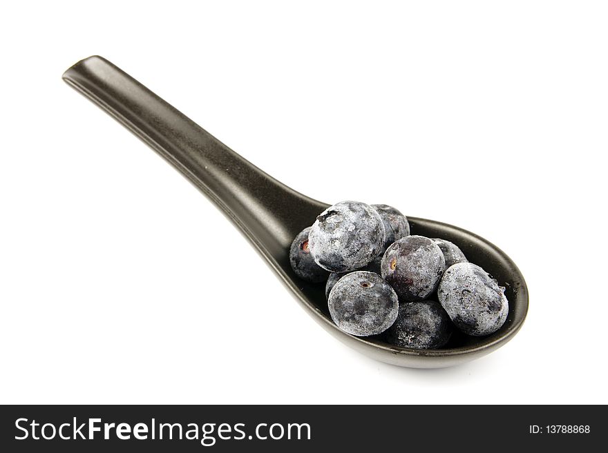 Blue ripe blueberries on s amll black spoon with a reflective white background. Blue ripe blueberries on s amll black spoon with a reflective white background