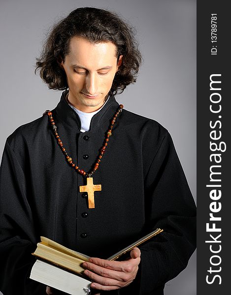 Praying priest with wooden cross and Bible