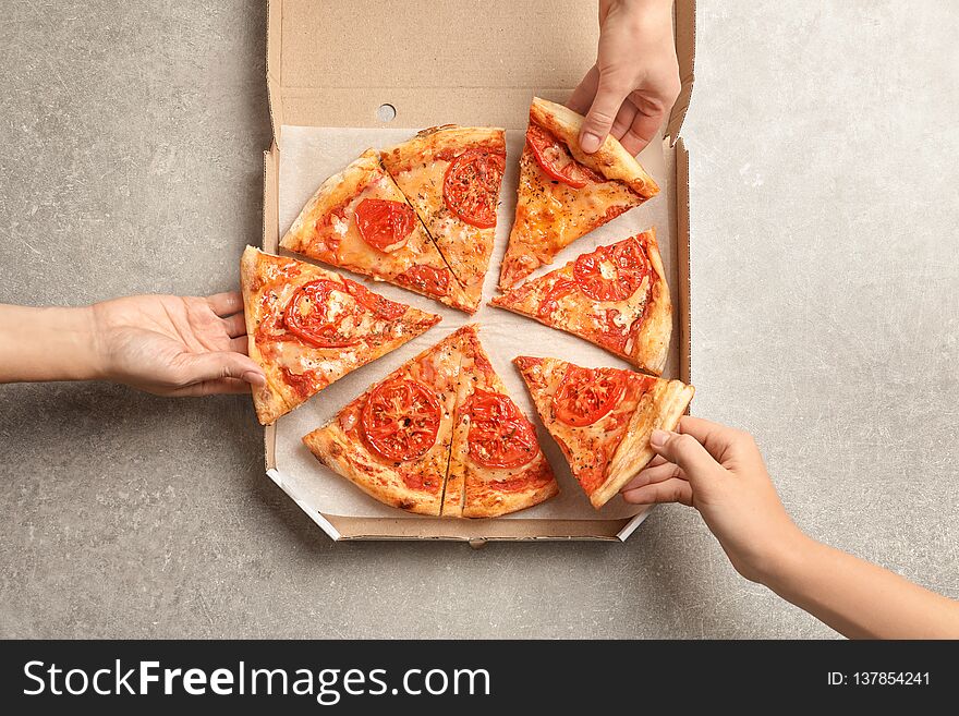 Young people taking slices of hot cheese pizza from cardboard box at table, top view. Food delivery