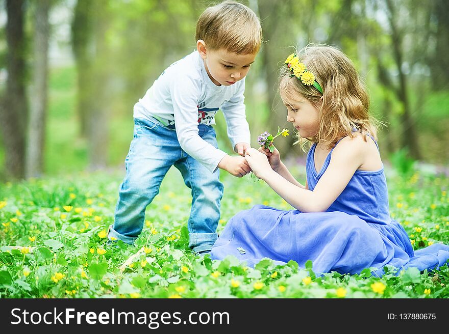 Brother and sister sit on the grass. Children`s games, leisure. Two children are sitting on green meadow and smile. Boy and girl