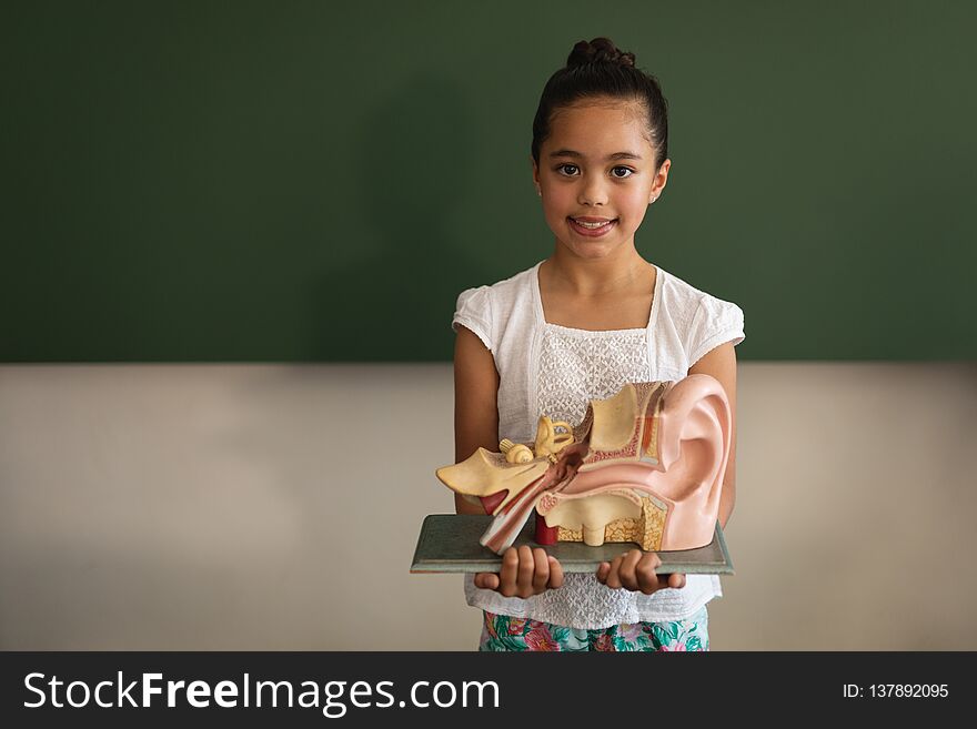 Front View Of Smiling Asian Schoolgirl Holding Anatomical Model And Looking At Camera In Classroom