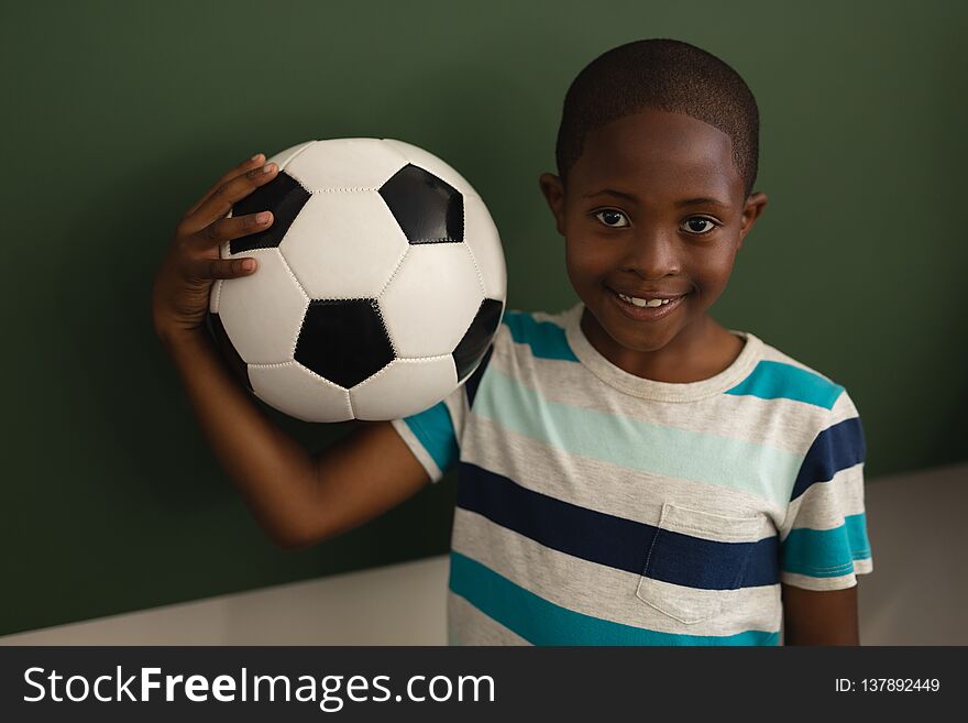 Front view of black schoolboy holding football and looking at camera in classroom of elementary school