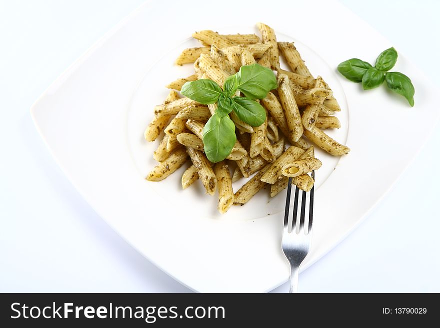 Penne with pesto decorated with basil on a plate with a fork