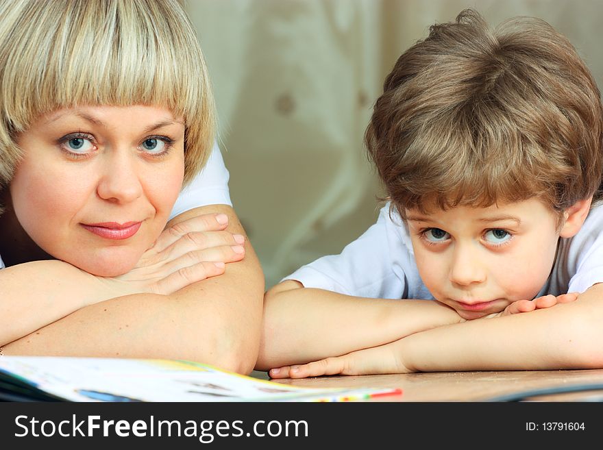 Woman and little boy lying down on the floor and reading a book. Woman and little boy lying down on the floor and reading a book