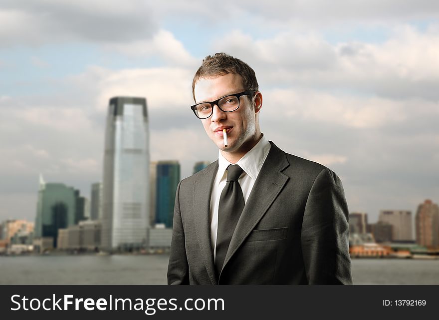 Young businessman with a cigarette in his mouth and cityscape on the background