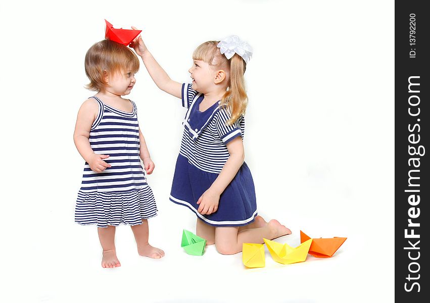 Two young sisters in sailor dresses with paper ships over white. Two young sisters in sailor dresses with paper ships over white