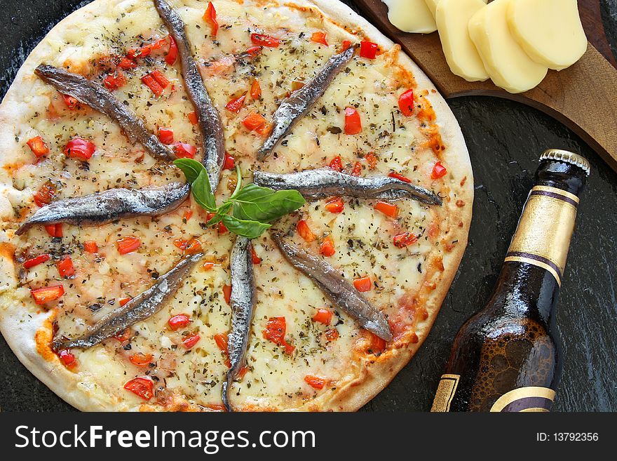 Anchovies pizza with a bottle of beer and ingredients