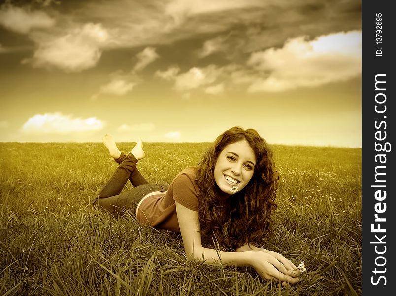 Smiling young woman lying on a meadow with a daisy in her mouth. Smiling young woman lying on a meadow with a daisy in her mouth