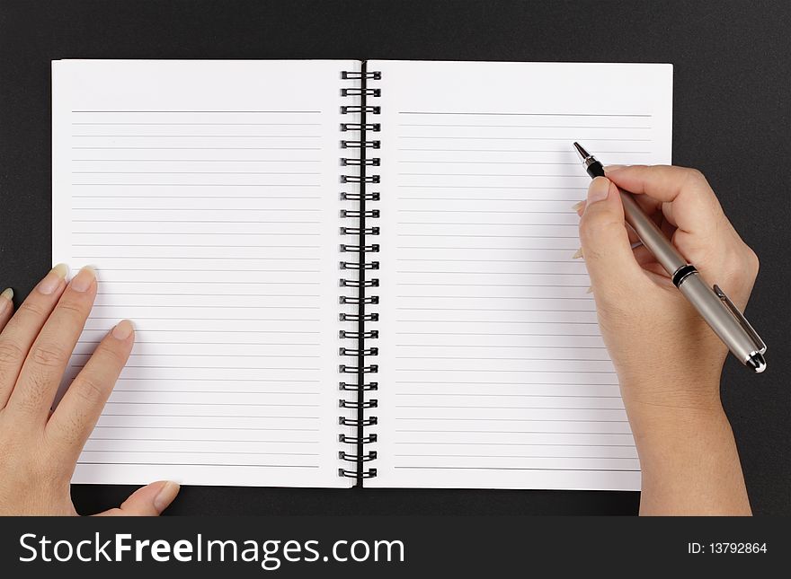 A pair of hands, a pen and a notebook on a black background. A pair of hands, a pen and a notebook on a black background