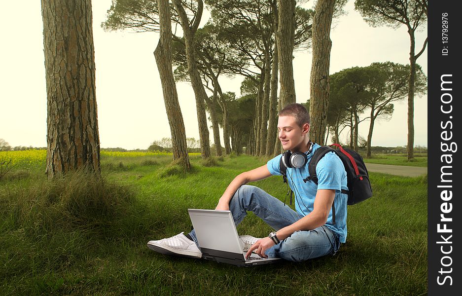 Young man sitting on a green meadow and using a laptop. Young man sitting on a green meadow and using a laptop