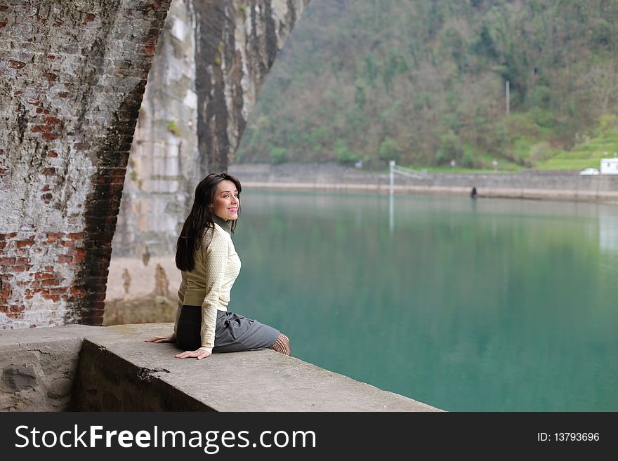 Smiling woman sitting under an ancient bridge