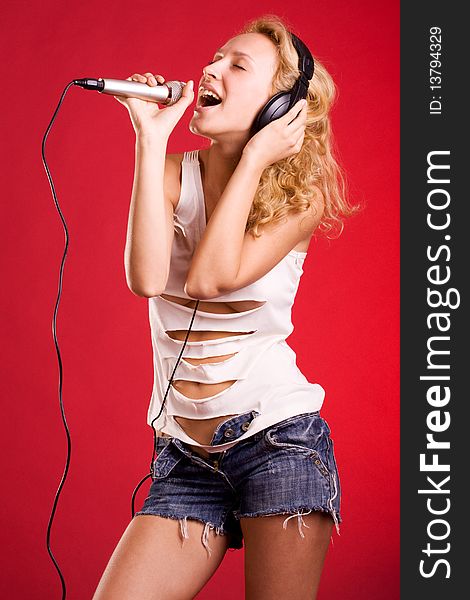 The girl with head-phones and a microphone sings on a red background. The girl with head-phones and a microphone sings on a red background