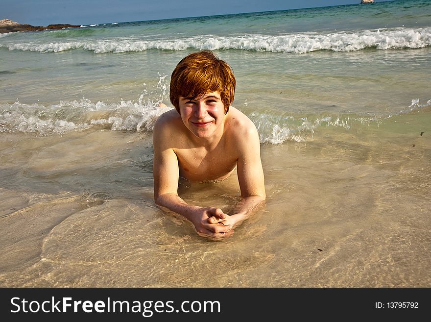 Boy in bathingsuit is lying at the beach and enjoying the saltwater with tiny waves and smiles. Boy in bathingsuit is lying at the beach and enjoying the saltwater with tiny waves and smiles