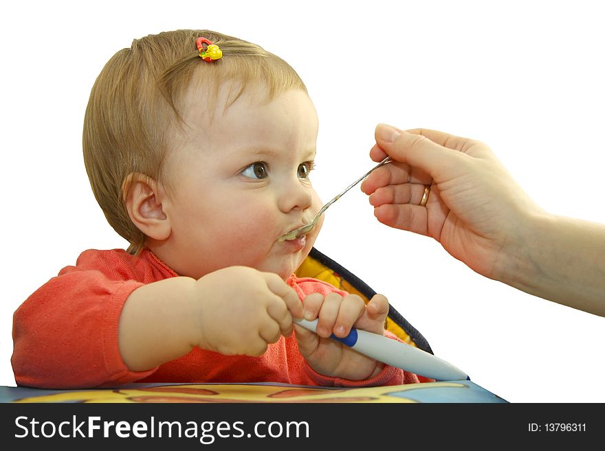 The child with a hairpin in hair sits at a table and he is fed with mum. The child with a hairpin in hair sits at a table and he is fed with mum