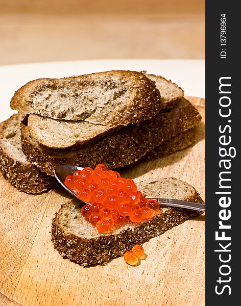 Red caviar in a spoon on a slice of rye bread. Red caviar in a spoon on a slice of rye bread