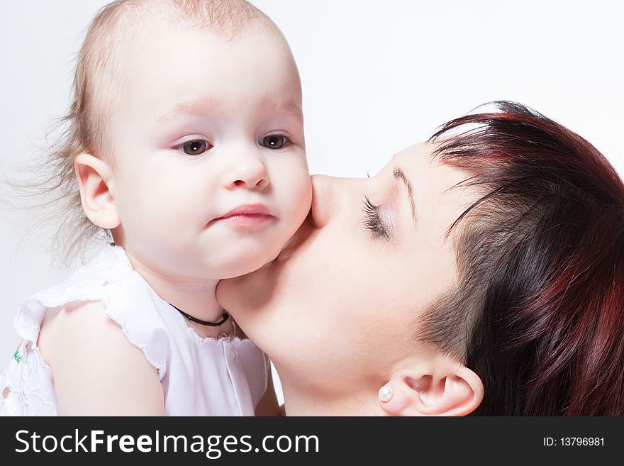 Young beautiful mother kissing cute curious baby, family portrait. Young beautiful mother kissing cute curious baby, family portrait