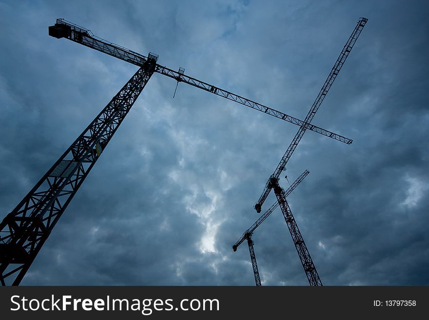 Three cranes under a stormy sky, shot from the ground up.