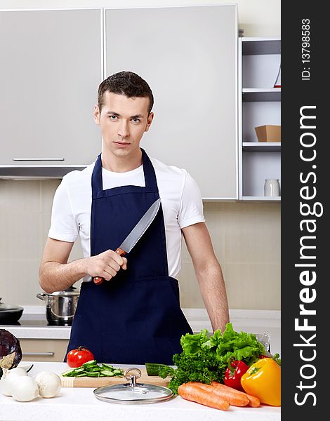 The young man in an apron with a knife at kitchen. The young man in an apron with a knife at kitchen