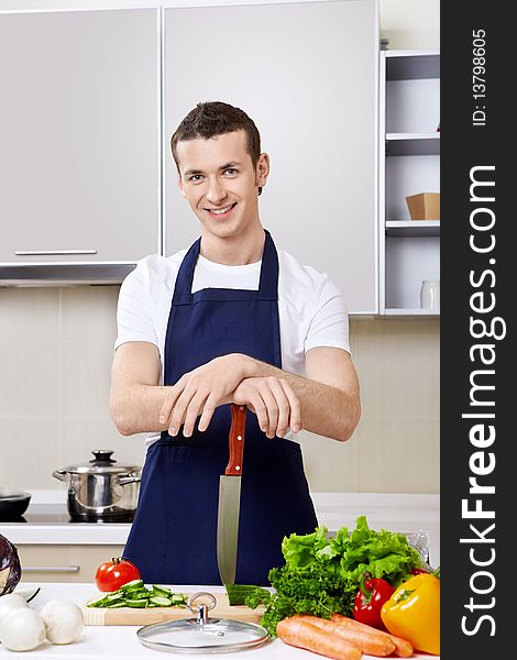 The young man in an apron with a knife at kitchen. The young man in an apron with a knife at kitchen