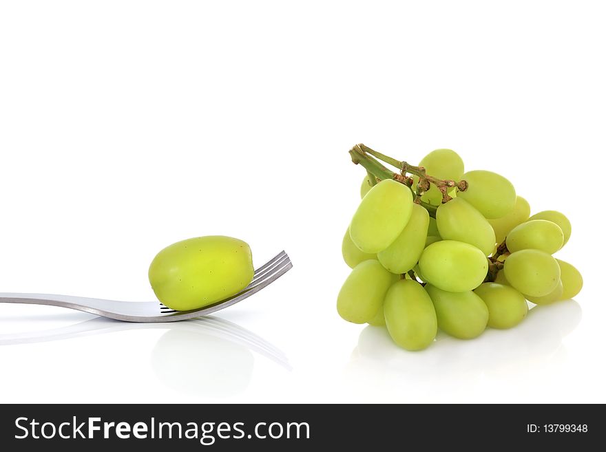 Bunch of green grapes with one on the end of a stainless steel fork, isolated over white background with reflection. Bunch of green grapes with one on the end of a stainless steel fork, isolated over white background with reflection.