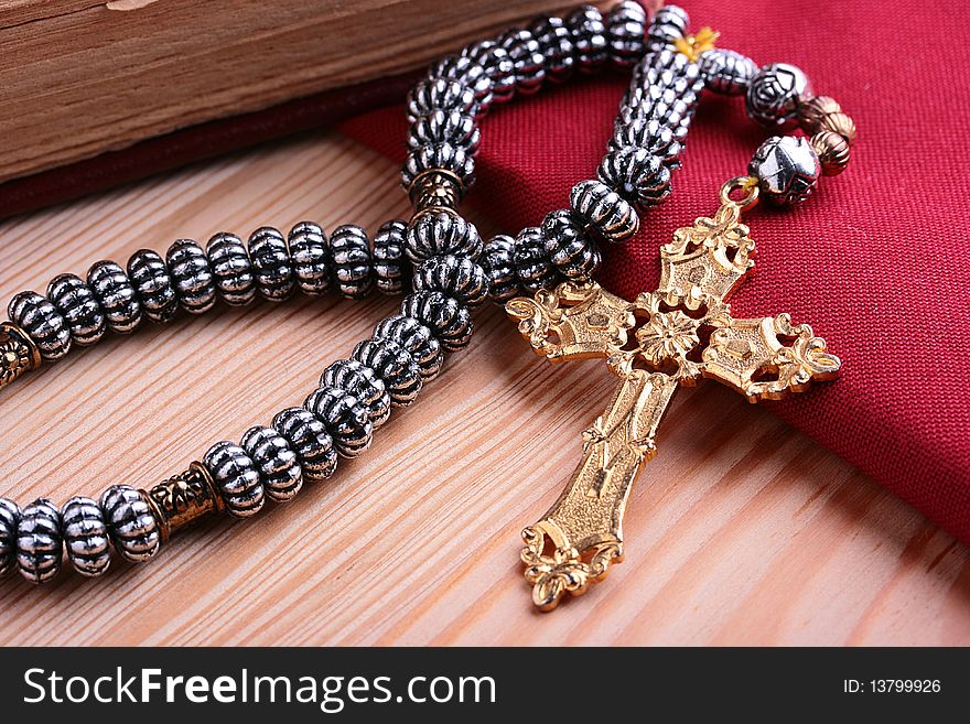 Religion. A cross with a chain against a wooden table and a red fabric. Religion. A cross with a chain against a wooden table and a red fabric.