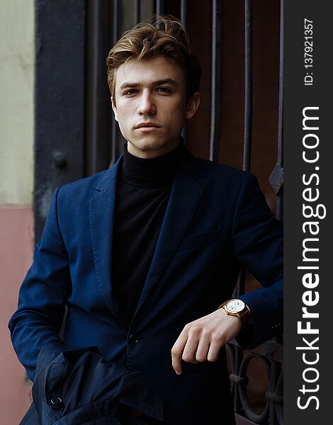 Portrait of an attractive man in a suit and a black sweater, close-up, on his hand a gold watch,brooding pose, looking at the camera.