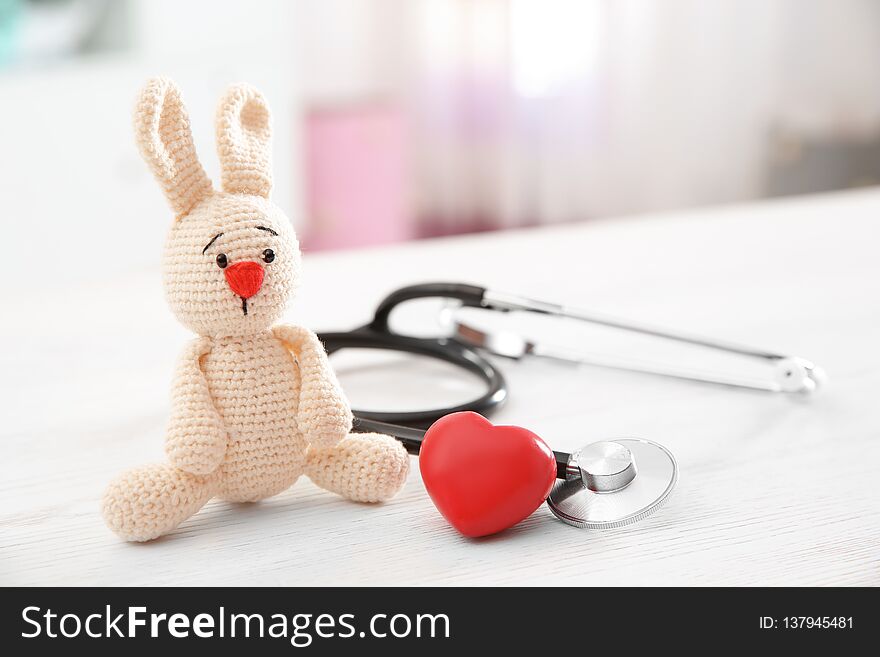 Toy bunny, stethoscope and heart on table indoors, space for text. Children`s doctor