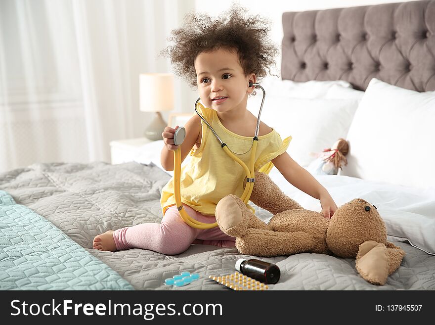 Cute African American child imagining herself as doctor while playing with stethoscope and toy bunny