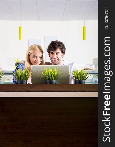 A beautiful young couple sitting in a coffee shop and using a laptop. A beautiful young couple sitting in a coffee shop and using a laptop