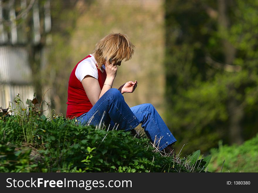 The girl with the phone sitting on a grass