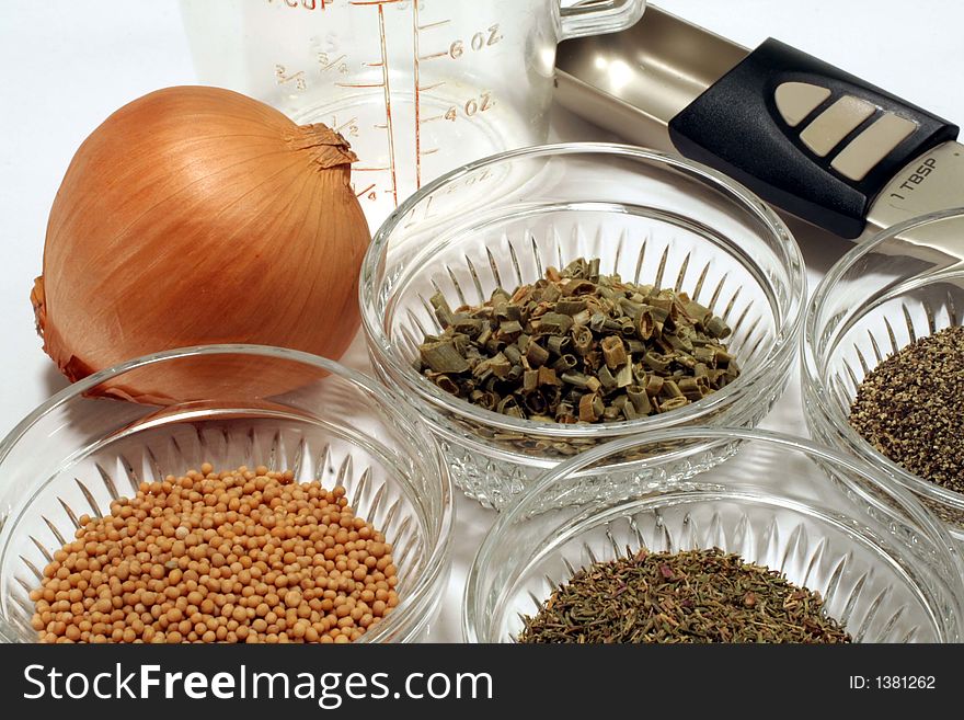 This is a closeup of various cooking ingredients and spices, along with an onion, measuring cup, and measuring spoon.