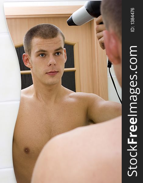 Reflexion of young man in the bathroom's mirror with hair drier