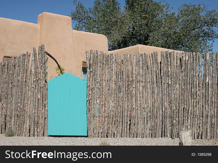 Turquoise gate with wooden pole fence and stucco building in the background. Turquoise gate with wooden pole fence and stucco building in the background