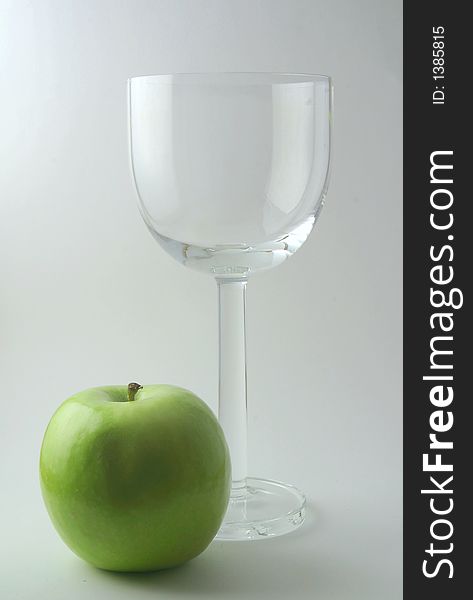 An empty wine glass and a green apple. An empty wine glass and a green apple