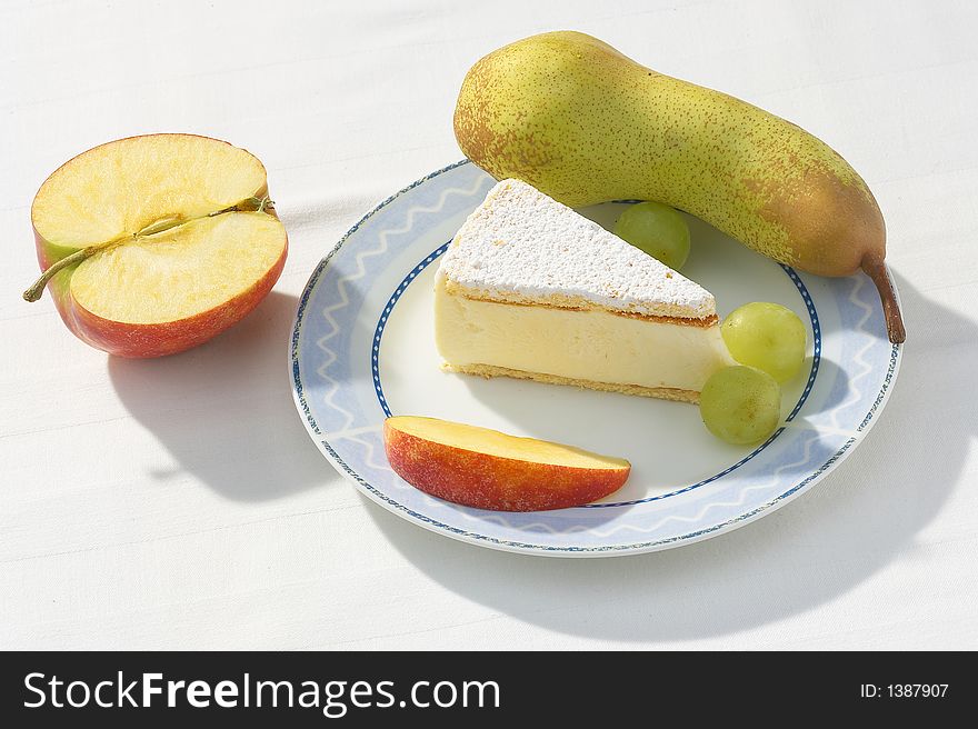 A piece of cheese cake together with a apple and a  pear on a white plate. A piece of cheese cake together with a apple and a  pear on a white plate