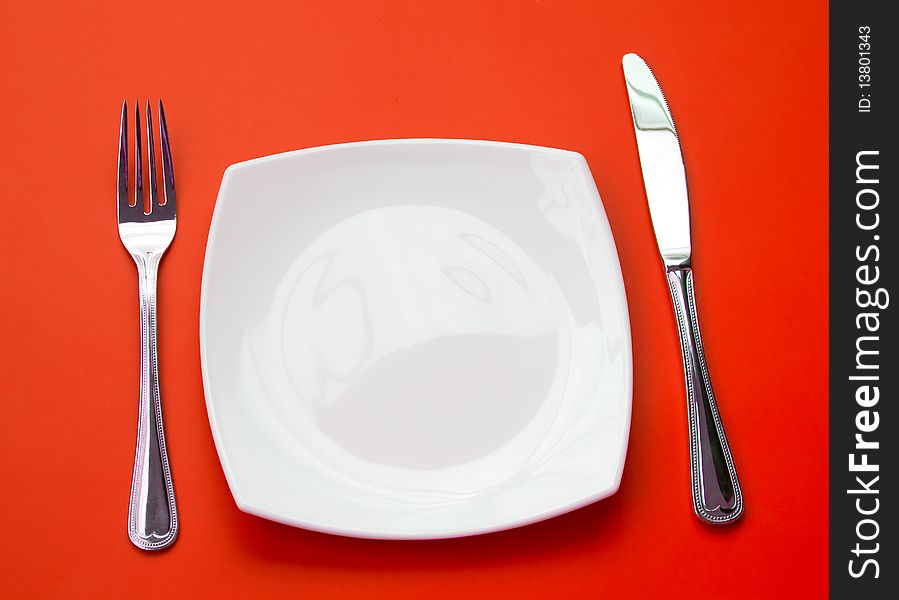 Knife, square white plate and fork on red background. Knife, square white plate and fork on red background