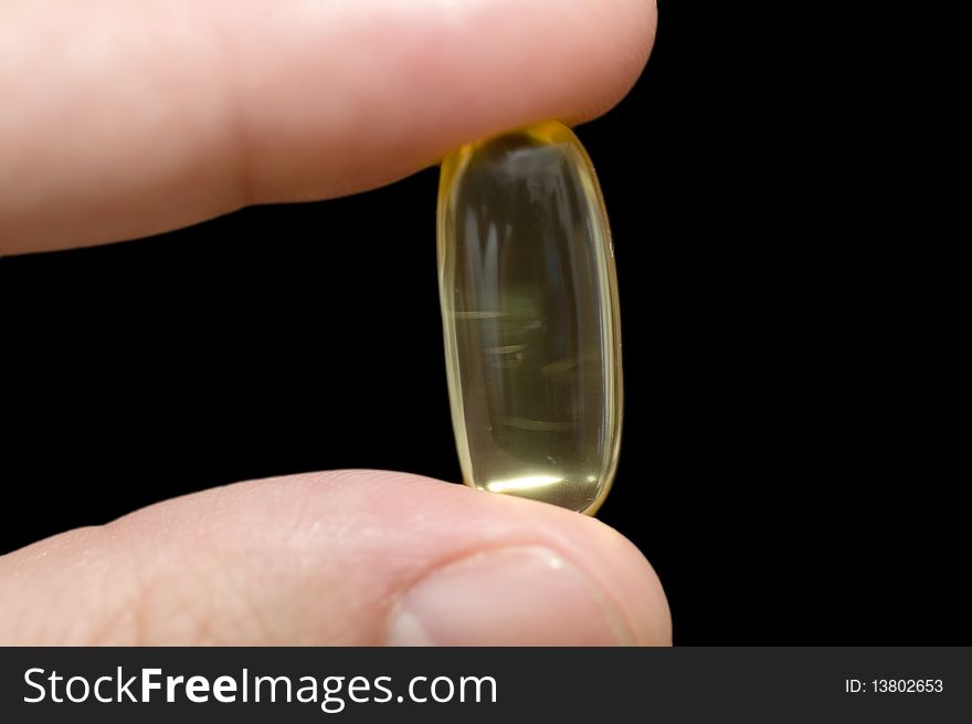 Hand holding a pill on black background