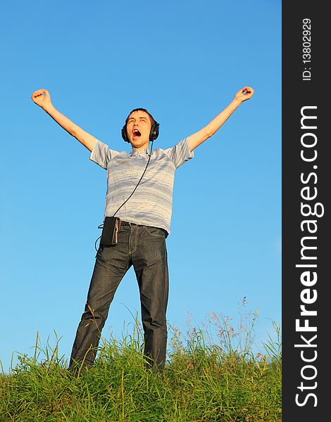 One handsome man is standing on a meadow with raised hands. headphones on his hand.