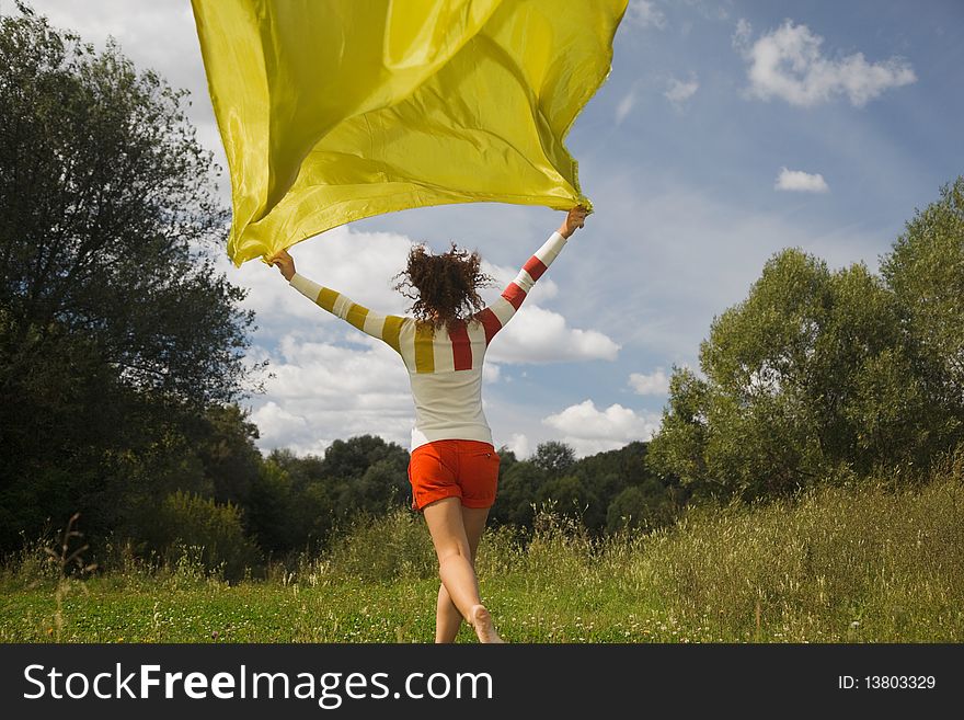 Young woman in sunny summer day runnig with yellow fabric in hand, whiffle fabric. Young woman in sunny summer day runnig with yellow fabric in hand, whiffle fabric