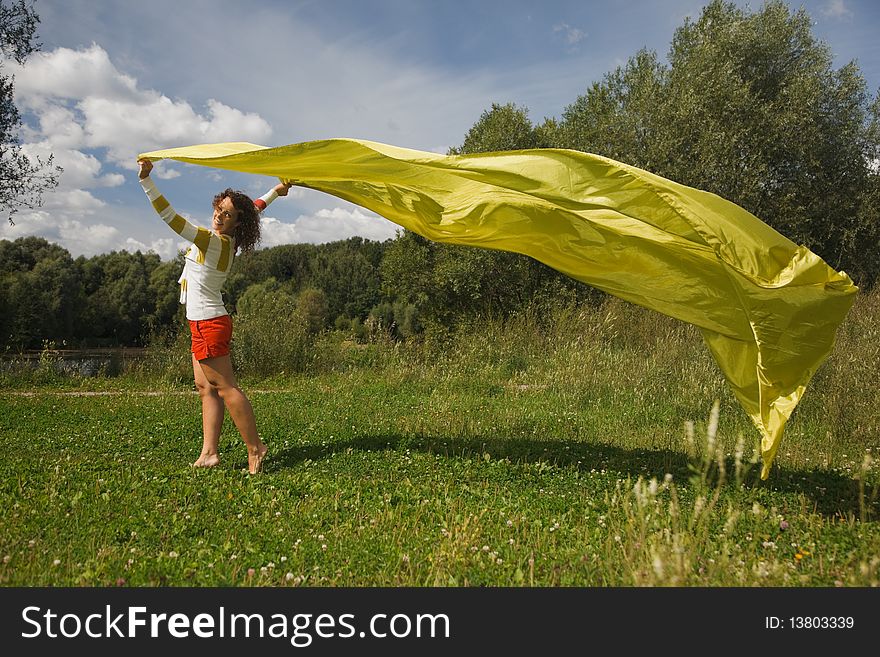 Young woman in sunny summer day holds in a hand developing on a wind a yellow fabric. looking in camera. Young woman in sunny summer day holds in a hand developing on a wind a yellow fabric. looking in camera