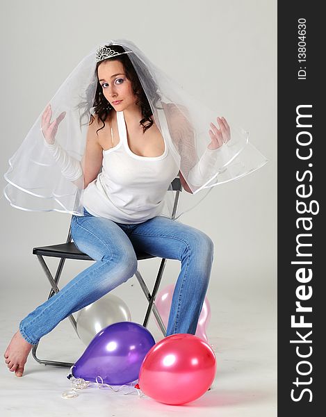 Portrait of the young girl sitting on a chair in jeans and a white vest. The bride in a veil prepares for wedding