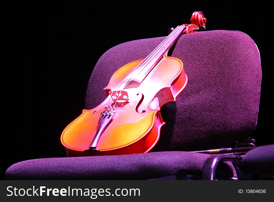 Abandoned violin in purple light on a chair