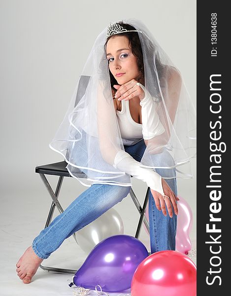 Portrait of the young girl sitting on a chair in jeans and a white vest. The bride in a veil prepares for wedding