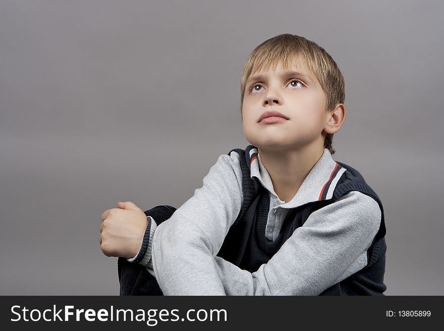 Dreaming and relaxing blond caucasian teenager boy with eyes lifted and hands crossed in front isolated over gray background. Dreaming and relaxing blond caucasian teenager boy with eyes lifted and hands crossed in front isolated over gray background