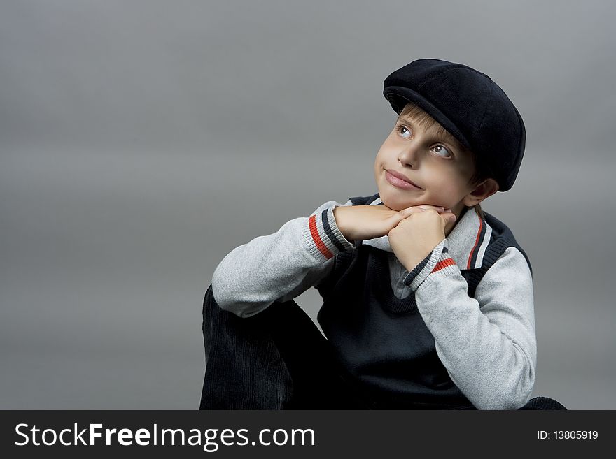 Cute teenager boy in old school cap sitting with hands crossed in front and smiling with natural nice smile isolated over gray background. Cute teenager boy in old school cap sitting with hands crossed in front and smiling with natural nice smile isolated over gray background