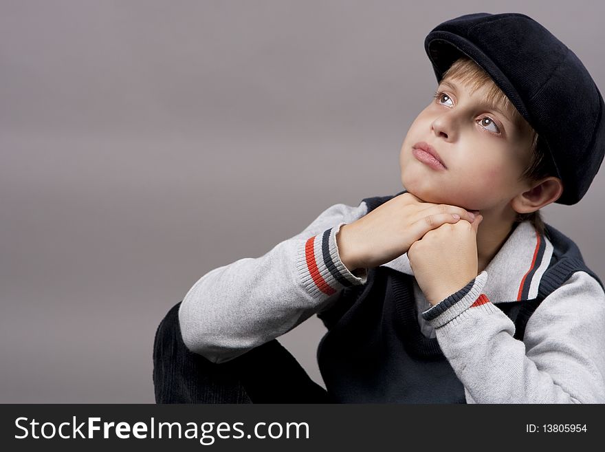 Relaxing and calm teenager boy in old cap sitting with hands crossed in front and looking up isolated over gray background. Relaxing and calm teenager boy in old cap sitting with hands crossed in front and looking up isolated over gray background