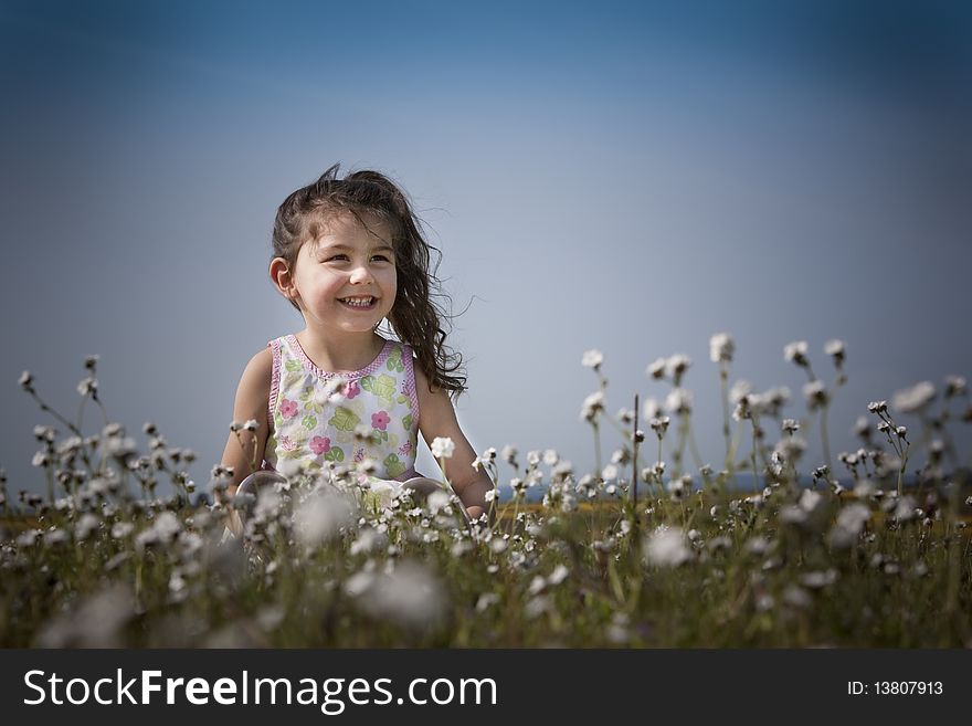 Little girl sitting in the white flowers smiling and happy. Little girl sitting in the white flowers smiling and happy