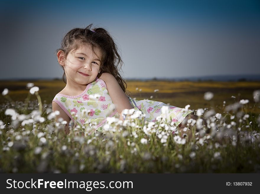 Little girl sitting in a field of white flowers smiling and happy. Little girl sitting in a field of white flowers smiling and happy