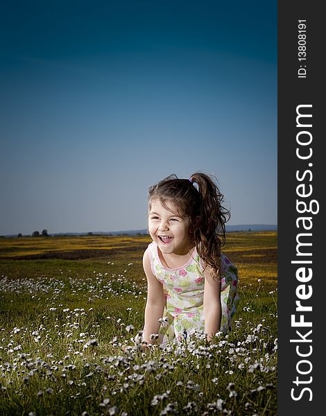 Little girl sitting in a field of white flowers laughing. Little girl sitting in a field of white flowers laughing