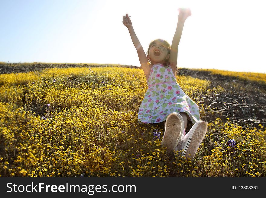Little girl sitting in a field of yellow flowers with her hands in the air. Little girl sitting in a field of yellow flowers with her hands in the air